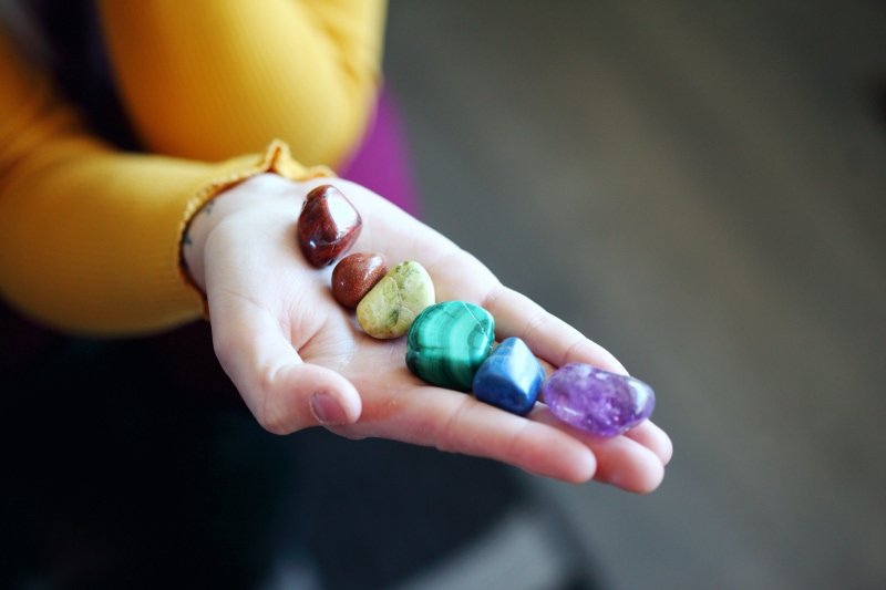Una donna tiene in mano 7 pietre colorate che rappresentano i 7 chakra dello yoga